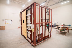 Prefabrykowany moduł łazienkowy z drzwiami z OSB i instalacją sanitarną na ramie.
